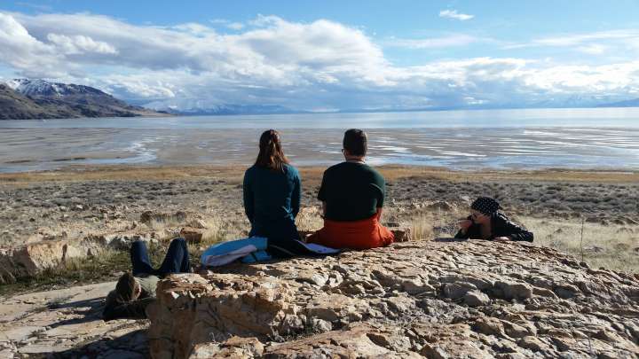 two people sitting on a rock with their backs to the camera looking out toward a salt flat